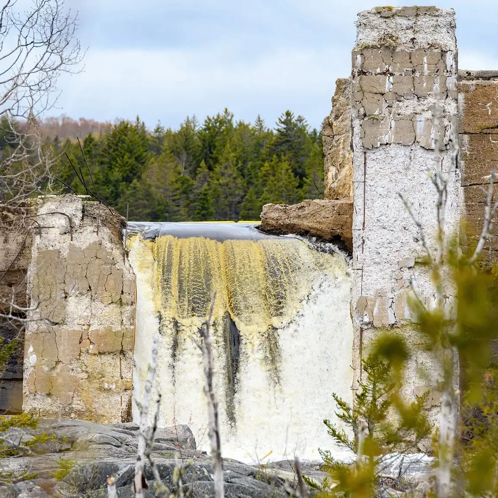The remains of an old concrete dam, water pouring over what is left of its crest.